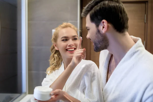 Smiling girlfriend applying cream on boyfriend face — Stock Photo