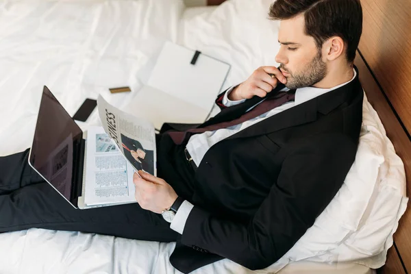 Blick aus der Vogelperspektive auf Geschäftsmann, der im Hotelzimmer auf dem Bett liegt und Zeitung liest — Stockfoto