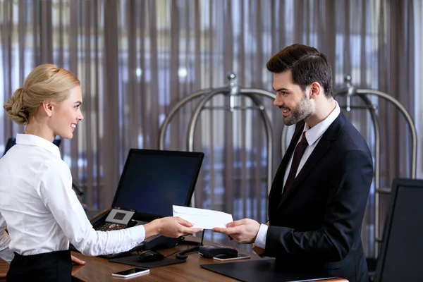 Lächelnde Empfangsdame übergibt Umschlag an Geschäftsmann im Hotel — Stockfoto