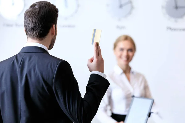 Vista trasera del hombre de negocios mostrando tarjeta de crédito a la recepcionista en el hotel — Stock Photo