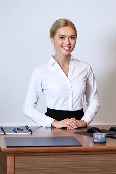 Smiling attractive receptionist standing at reception desk in hotel — Stock Photo