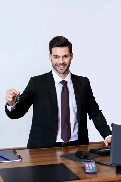 Smiling handsome receptionist holding key at reception desk — Stock Photo