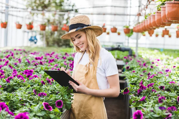 Young female owner of glasshouse with clipboard filling order of flowers — Stock Photo