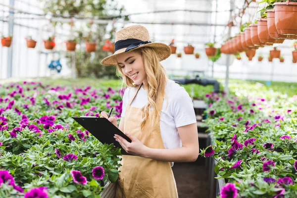 Giovane donna proprietaria di serre con blocco appunti ordine di riempimento di fiori — Foto stock