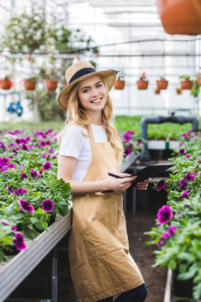 Blonde woman with clipboard filling order of flowers in greenhouse — Stock Photo