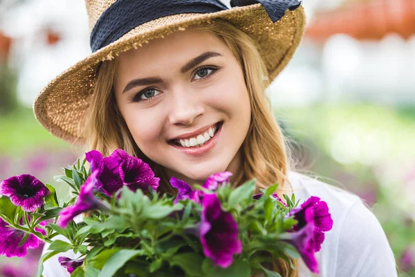 Femme blonde tenant des fleurs violettes en serre — Photo de stock