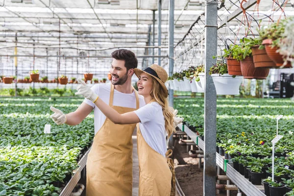 Donna bionda e bell'uomo in grembiuli che parlano tra fiori in serra — Foto stock