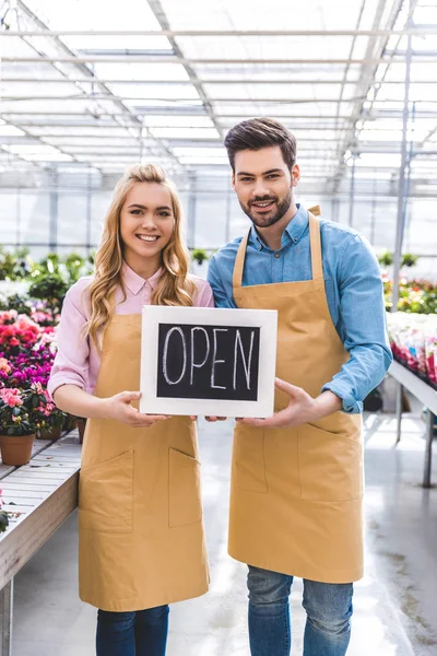 Couple of gardener holding Open board by flowers in greenhouse — Stock Photo