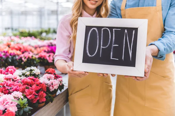 Close-up view of Open board in hands of owners of greenhouse standing among flowers — Stock Photo