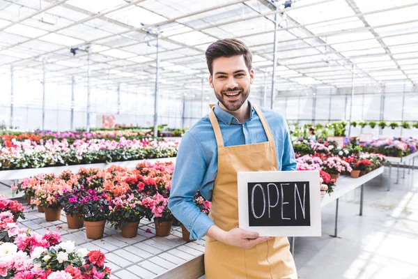 Male owner of greenhouse with Open board by flowers — Stock Photo