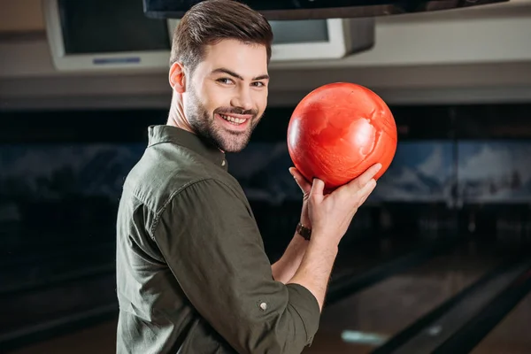 Sonriente joven sosteniendo la bola de bolos y mirando a la cámara - foto de stock