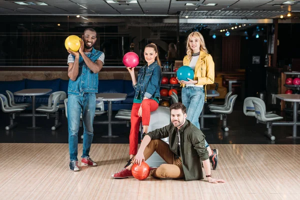 Happy young friends posing with balls at bowling club — Stock Photo