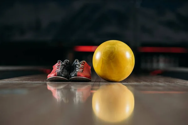 Bola de boliche amarelo com sapatos no beco no clube — Fotografia de Stock