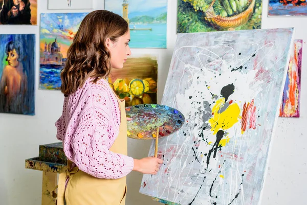 Side view of beautiful female artist looking at canvas in workshop — Stock Photo