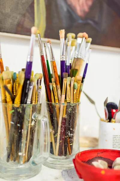 Painting brushes in glasses on table in workshop — Stock Photo