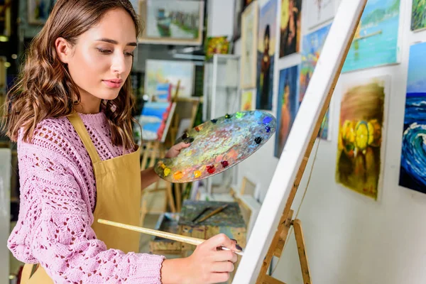 Vista lateral de la hermosa pintura artista femenina sobre lienzo en el taller - foto de stock