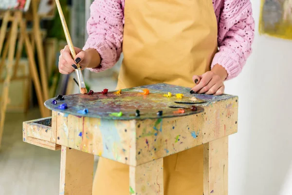 Imagen recortada de artista femenina aplicando pinturas en la paleta en el taller - foto de stock