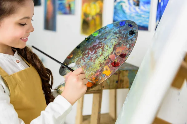 Enfant prenant de la peinture de la palette dans l'atelier de l'école d'art — Photo de stock