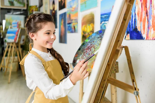 Vue latérale de la peinture enfant souriante dans l'atelier de l'école d'art — Photo de stock