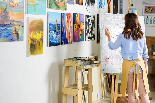 Vista posteriore della pittura di artista donna mancina su tela in officina — Foto stock