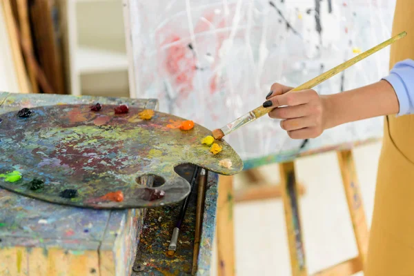 Cropped image of left-handed artist taking paint from palette in workshop — Stock Photo