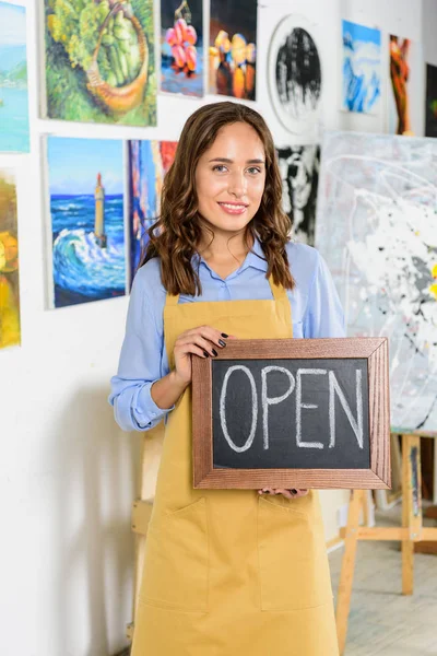 Attrayant artiste femme tenant enseigne avec mot ouvert dans l'atelier — Photo de stock