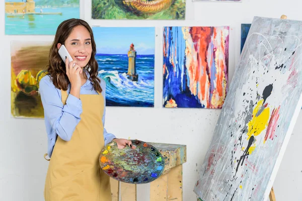 Hermosa artista femenina hablando por teléfono inteligente en el taller - foto de stock