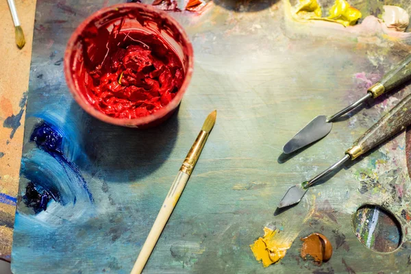 Pinceles para pintar, paleta y pintura con póster rojo sobre mesa de madera en taller - foto de stock