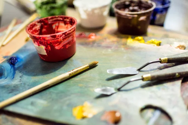 Pinceaux à peindre, palette et affiches peintures sur table en bois dans l'atelier — Photo de stock