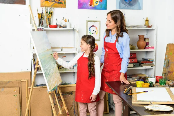 Teacher watching how pupil painting on canvas in workshop of art school — Stock Photo