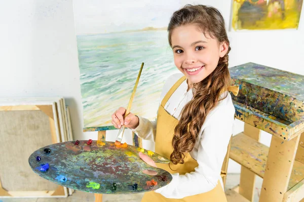 Kid holding painting brush and palette in workshop of art school — Stock Photo