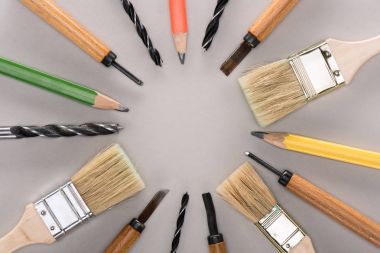 top view of various paint brushes, pencils, chisels and drills on grey