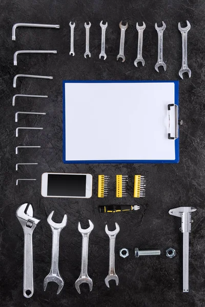 Vista superior del conjunto de herramientas de construcción, smartphone y portapapeles en blanco — Foto de Stock