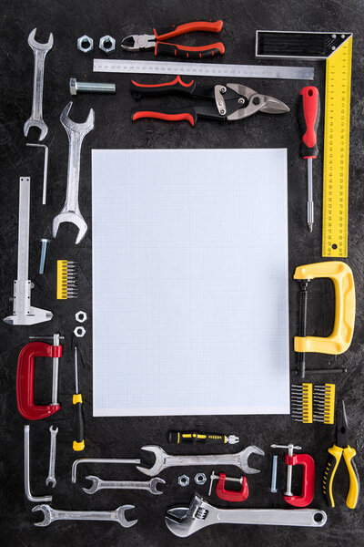 top view of set of various work tools and blank paper on black