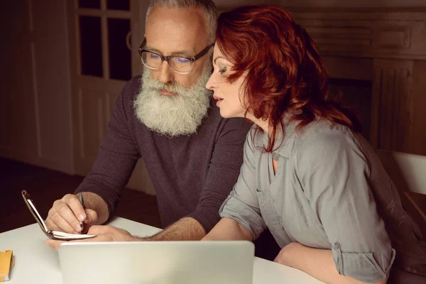 Ehepaar mittleren Alters schaut auf Notizbuch — Stockfoto