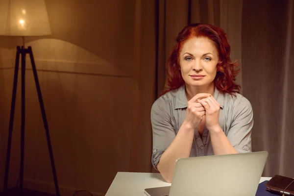 Reife Frau sitzt am Tisch neben Laptop — Stockfoto