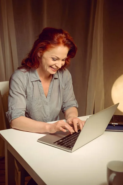 Χαμογελώντας ώριμη γυναίκα που εργάζεται σε φορητό υπολογιστή — Φωτογραφία Αρχείου