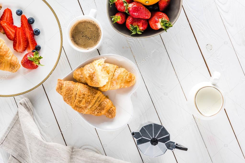 croissants with coffee and strawberries on wooden tabletop
