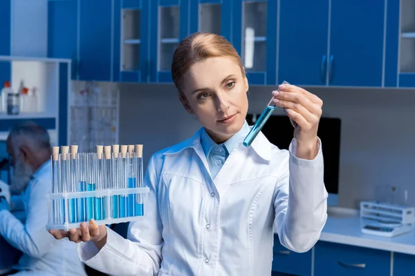 Científico en bata de laboratorio mirando tubo — Foto de Stock