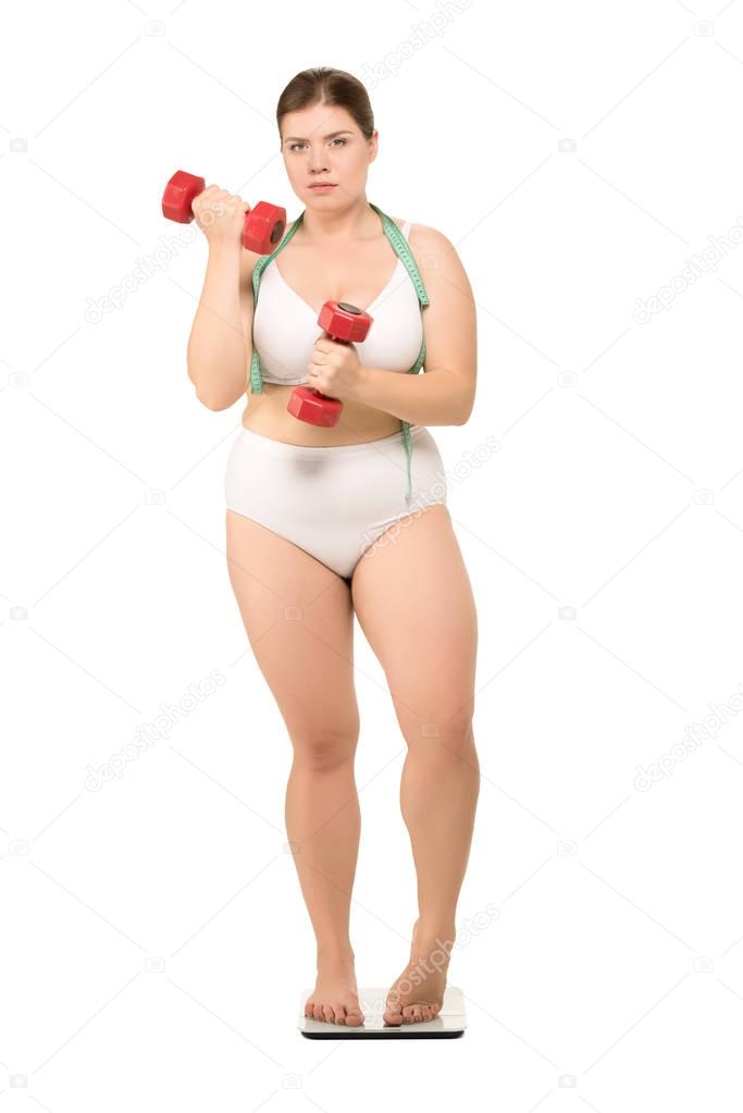 overweight woman with dumbbells on scales