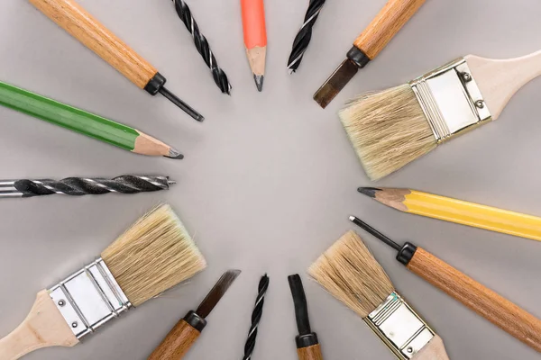 Vista superior de várias escovas de tinta, lápis, cinzentos e brocas em cinza — Fotografia de Stock