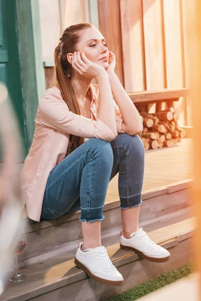 Mujer pensativa sentada en el porche - foto de stock