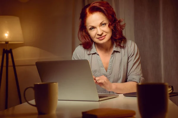 Женщина работает на ноутбуке и смотрит в камеру — стоковое фото