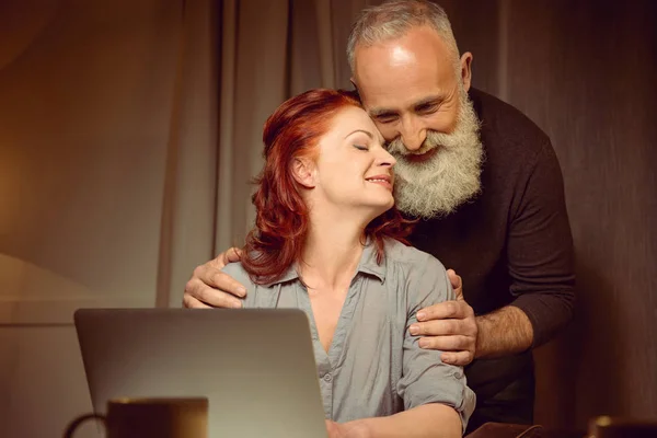 Abbracciando coppia di mezza età vicino laptop — Foto stock