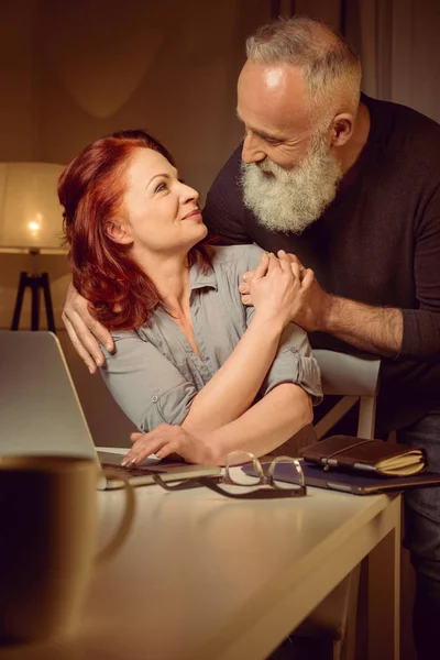 Abrazando pareja cerca del ordenador portátil en casa - foto de stock