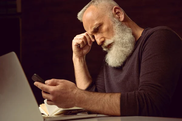 Mann sitzt am Tisch und benutzt Smartphone — Stockfoto