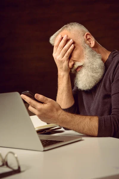 Hombre sosteniendo teléfono inteligente con facepalm - foto de stock