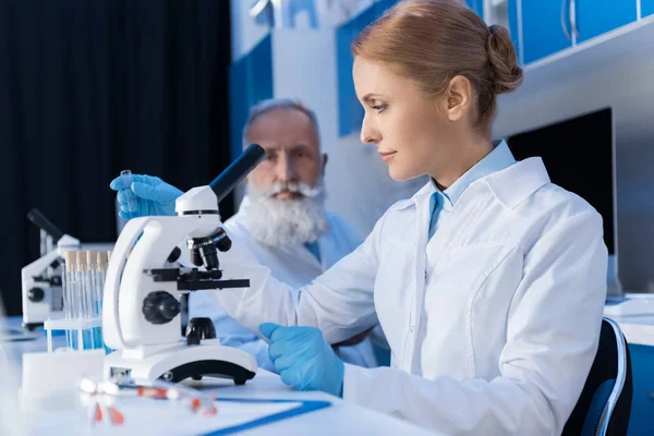 Frau im Laborkittel arbeitet mit Mikroskop — Stockfoto