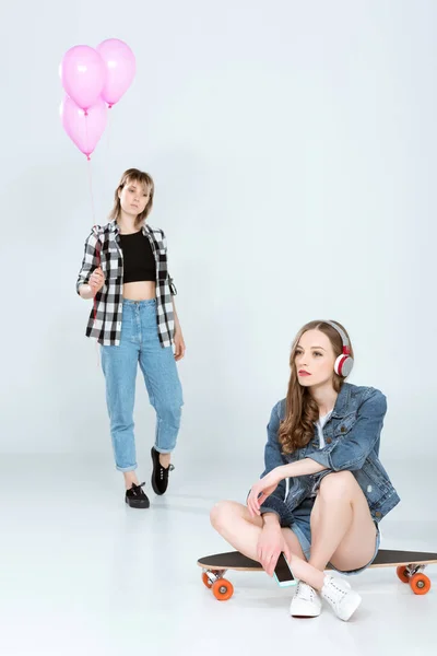 Mujeres jóvenes con monopatín y globos - foto de stock
