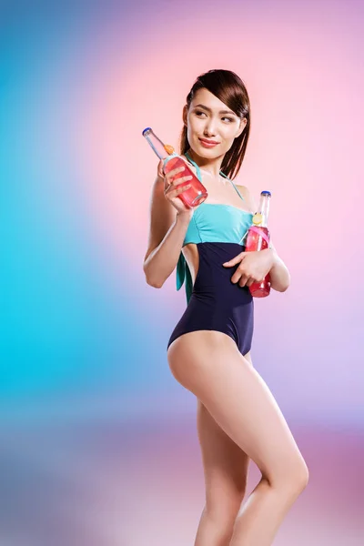 Chica en traje de baño sosteniendo botellas - foto de stock